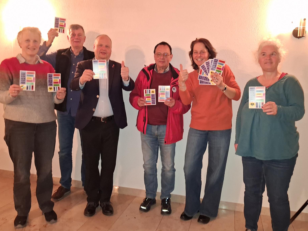 Gruppe von Menschen die Sticker-Postkarten der Aktion "Aufstehen für ..." zeigen