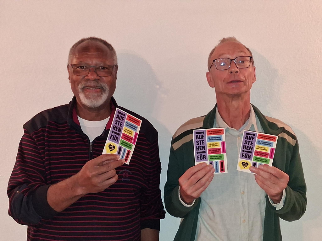 2 Männer, die Sticker-Postkarten der Aktion "Aufstehen für ..." zeigen