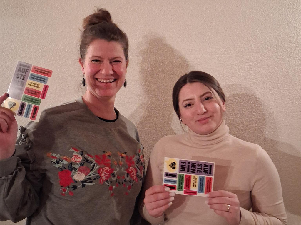 2 Frauen, die Sticker-Postkarten der Aktion "Aufstehen für ..." zeigen