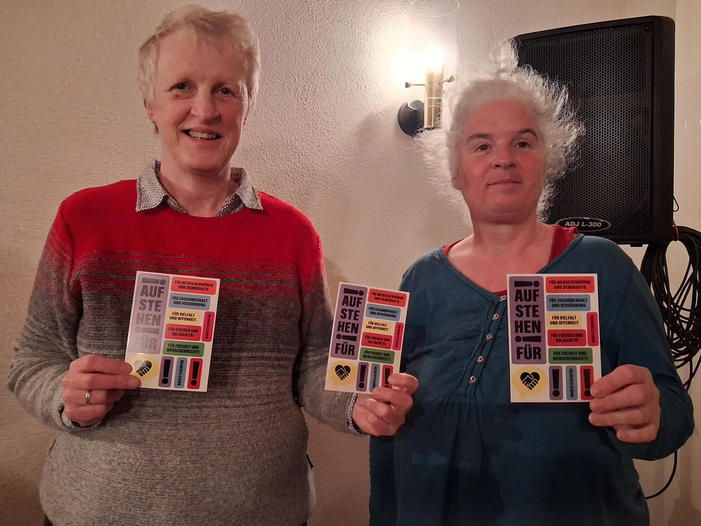 2 Frauen, die Sticker-Postkarten der Aktion "Aufstehen für ..." zeigen